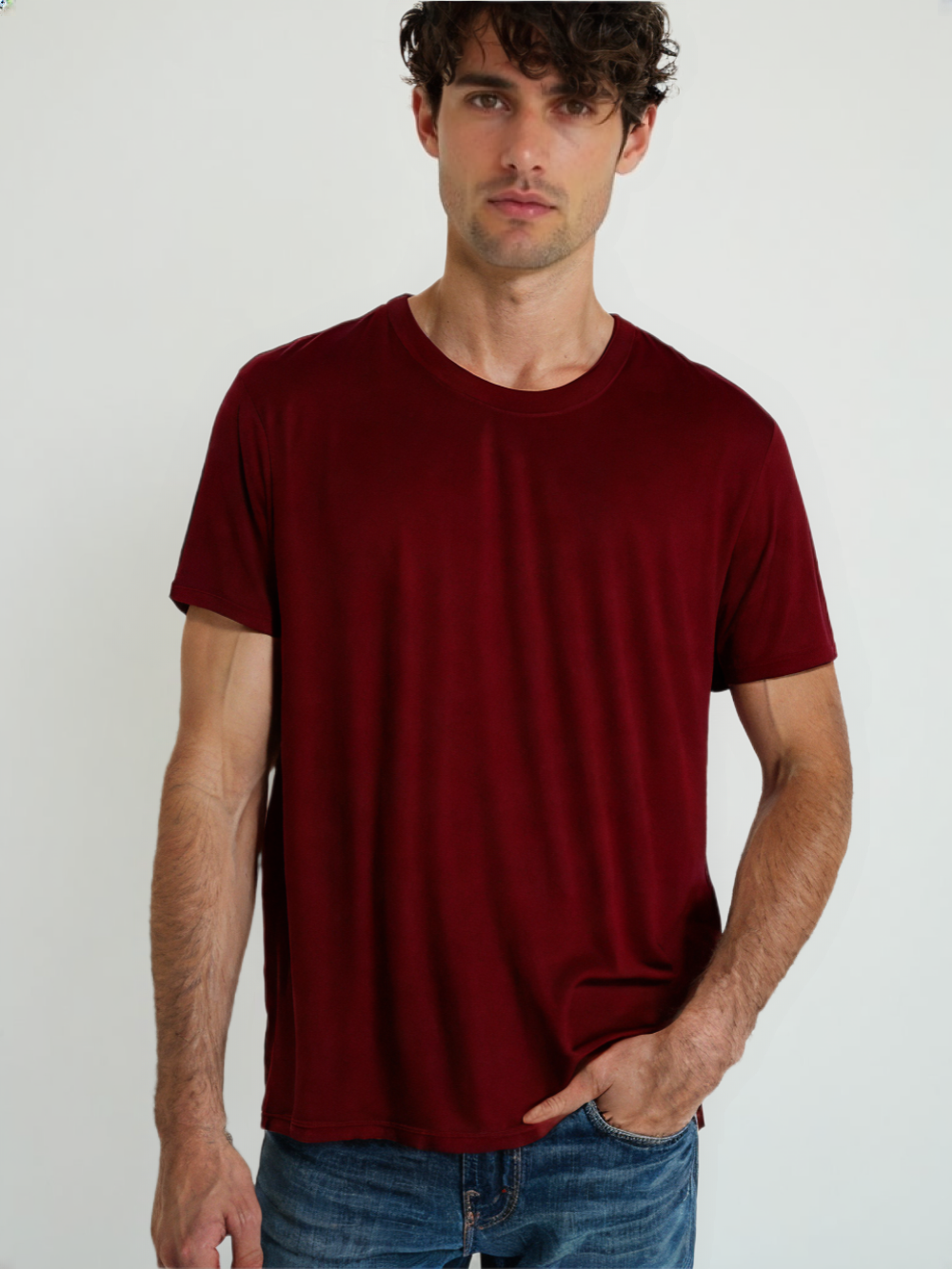 Man wearing a classic red t-shirt for men paired with blue jeans standing against a white background