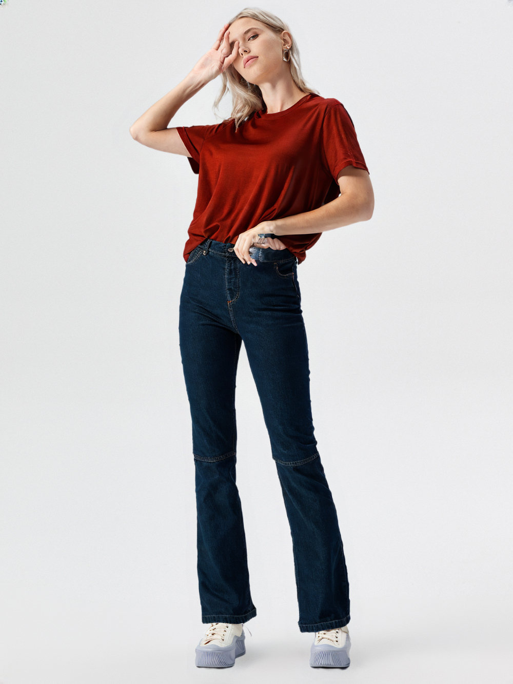 Woman wearing a classic red t-shirt for men styled with dark blue jeans and white sneakers
