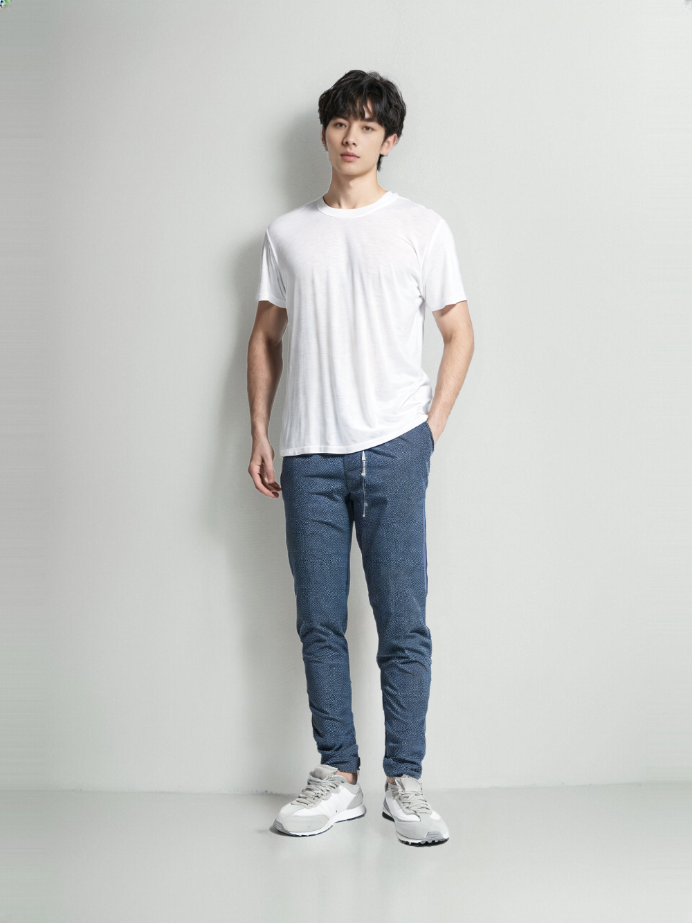 Man wearing a classic white t-shirt paired with blue jeans and white sneakers against a plain background